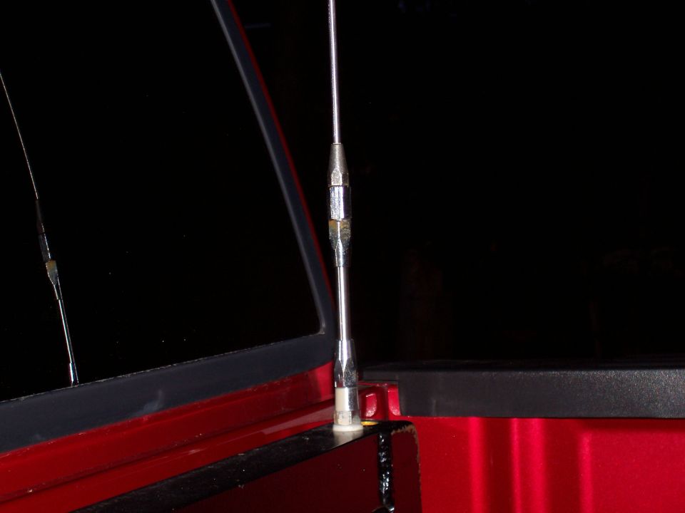 Close-up of a chrome antenna mount on a red vehicle's body panel