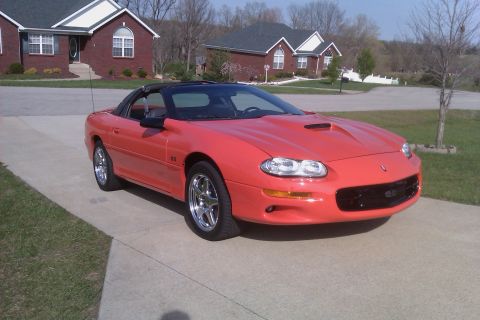 1999 Chevrolet Camaro - A red Chevrolet Camaro with an SS badge is parked in front of a suburban house.