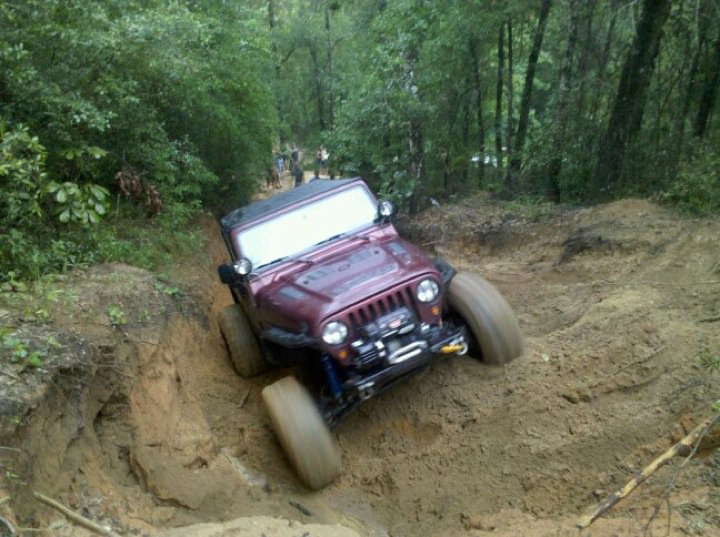 Maroon Jeep Wrangler struggling on a muddy off-road trail, front wheels turned