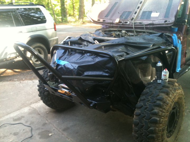 Freshly painted black tube front bumper on a maroon Jeep with body masked in plastic