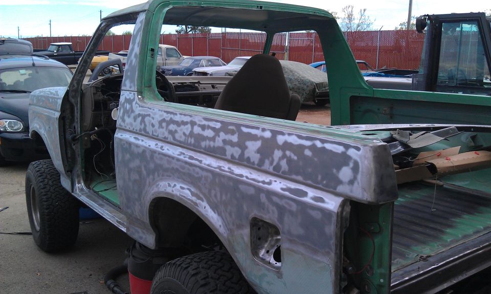 Green SUV body with primer, sanding marks, and removed door