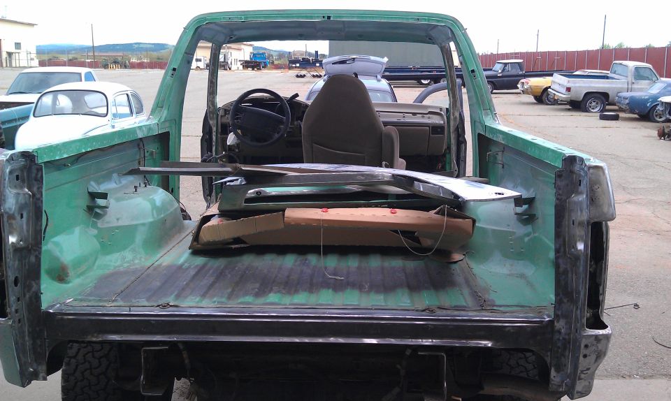 1995 Ford Bronco stripped down, showing interior and bed with parts inside. Green exterior paint is visible