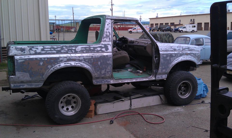 Side profile of a doorless Bronco sanded to bare metal and primer, tan seats visible