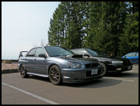 1998 Subaru Legacy - Two Subarus and a blue car parked outdoors with trees in the background.