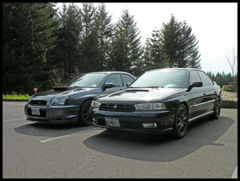 1998 Subaru Legacy - Two Subaru sedans are parked side-by-side in a paved lot with trees in the background.