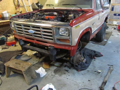 1984 Ford Bronco - A two-tone red and tan 1980 Ford Bronco's front end is visible with the hood open, indicating it is in a repair shop.