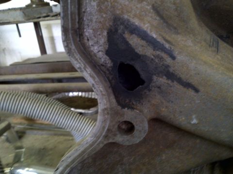 1979 Ford Bronco - Close-up of a corroded metal component, possibly from an exhaust system, showing a significant hole and dark residue.