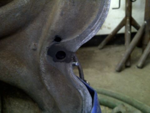 1979 Ford Bronco - A close-up view of a metal component, likely part of a vehicle's suspension system, with visible holes and a blue strap.