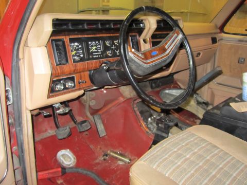 1984 Ford Bronco - The interior of this vehicle features a wood-grain dashboard and plaid seating, characteristic of 1980s Ford Broncos.
