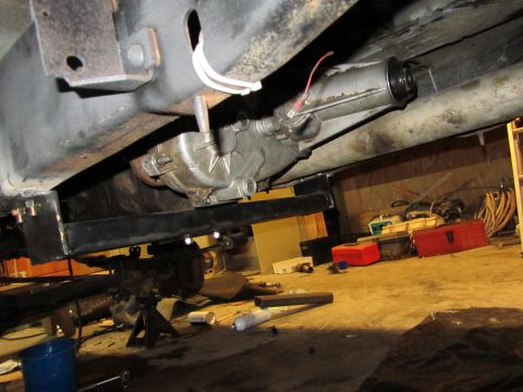 1984 Ford Bronco - The underside of a vehicle is shown, focusing on the transfer case and suspension parts, with tools scattered on the garage floor.
