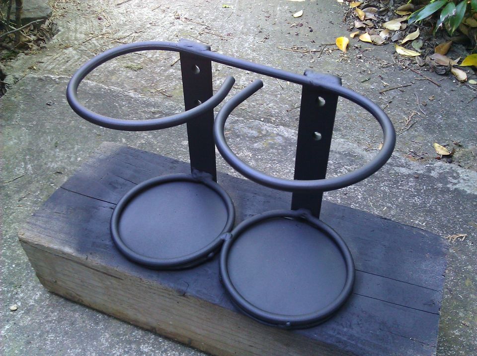 Black metal dual cup holder assembly with two large rings and two smaller circular bases, mounted on a wooden block