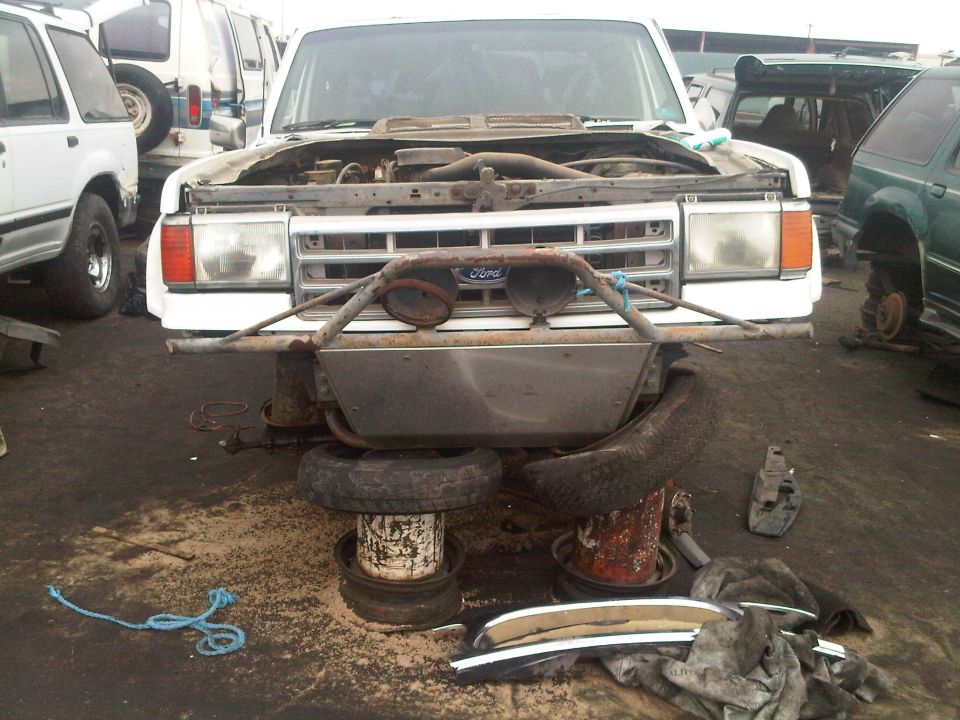 White Ford Bronco with hood open, aftermarket bumper, and missing tires