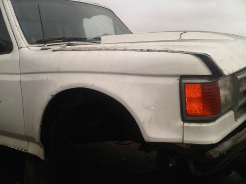 1986 Ford Bronco - Front corner view of a white truck, showing the fender, headlight, and part of the grille. The vehicle appears to be from around 1987.