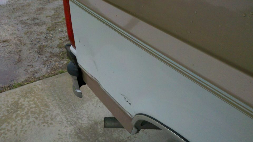 Close-up of white and tan rear quarter panel with scuff and paint chip above bumper