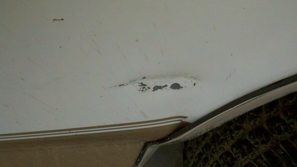 Close-up of dent and chipped paint exposing gray metal on white body panel of 1996 Ford Bronco