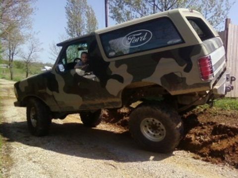 1995 Ford Bronco - This 1995 Ford Bronco sports a camouflage paint job and is captured in a three-quarter front view while navigating an off-road trail.