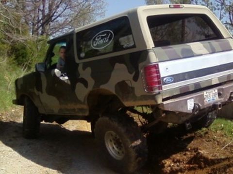 1995 Ford Bronco - Camouflaged Ford Bronco with lifted suspension on a dirt path.