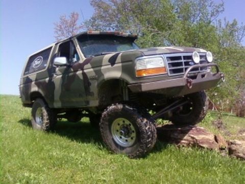 1995 Ford Bronco - This 1995 Ford Bronco is shown in a three-quarter front view, navigating over rocks on a grassy incline.