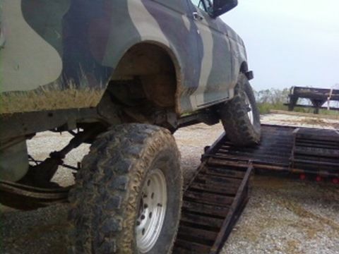1995 Ford Bronco - A camouflaged truck is being loaded onto a trailer using a ramp, showing its large tires and suspension.