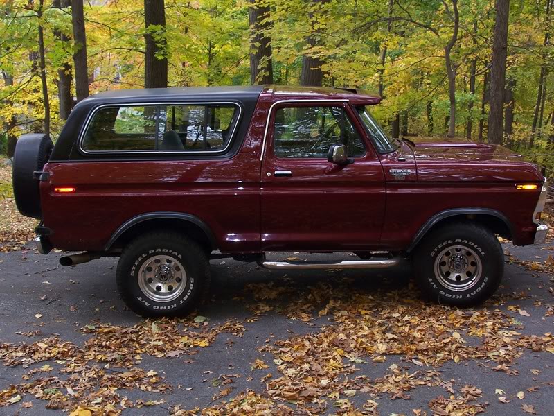 Maroon 1978 Ford Bronco with black top and spare tire on rear, parked on asphalt with fallen leaves