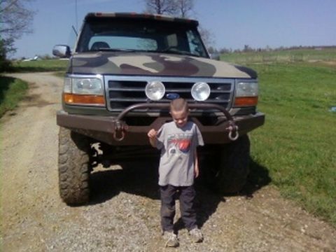 1995 Ford Bronco - Child poses in front of a 1995 Ford Bronco with custom camouflage paint and a heavy-duty bumper.