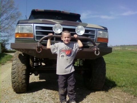 1995 Ford Bronco - A young boy poses in front of a heavily modified pickup truck with a camouflage paint scheme.
