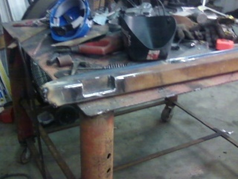 Metal rock sliders on a workbench with welding equipment and a blue hard hat