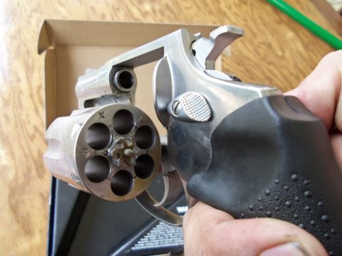 2000 Mercury Grand Marquis - A silver revolver with a black grip is held in a hand, showing the open cylinder with six chambers.