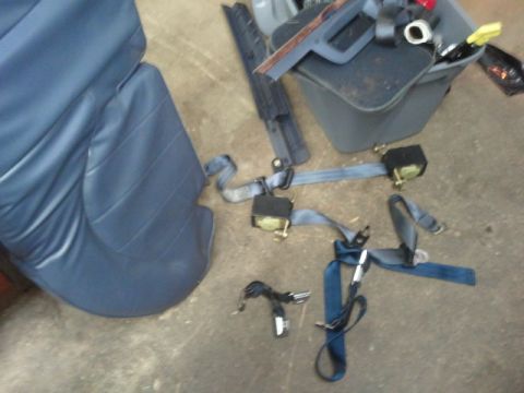 1998 Ford Crown Victoria - Blue seat belt assemblies with gold-toned retractor mechanisms and buckle stalks laid out on a concrete garage floor next to a removed blue…