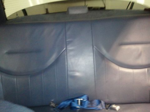 1998 Ford Crown Victoria - Rear bench seat of a sedan upholstered in dark blue vinyl, shot from inside the car with the rear parcel shelf and window above. Blue seat…