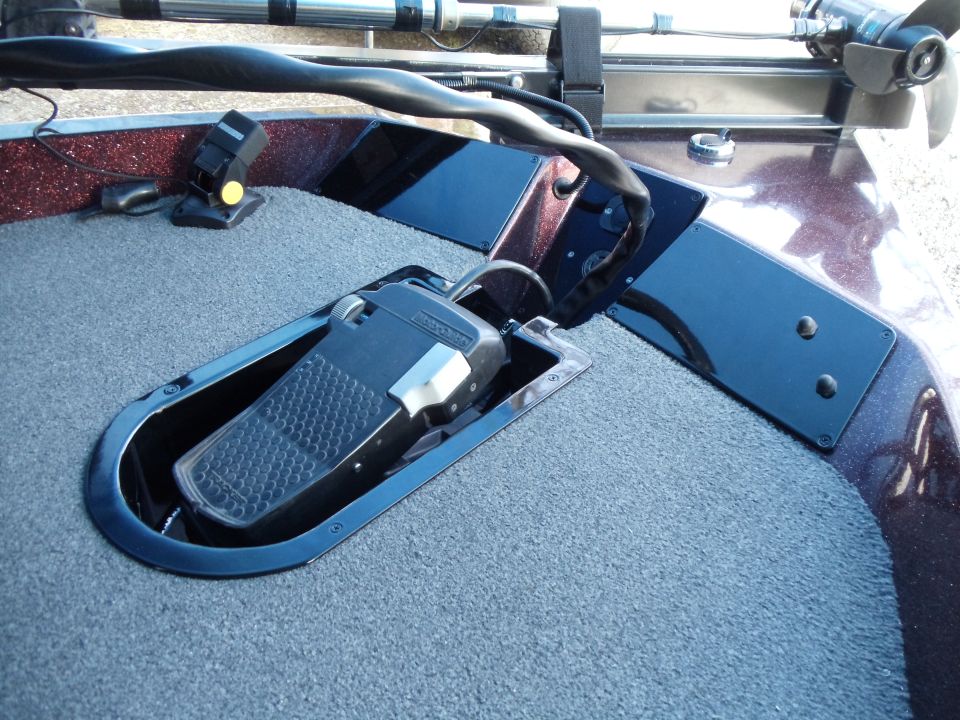 Foot-control pedal recessed in the carpeted bow deck of a red metal-flake bass boat