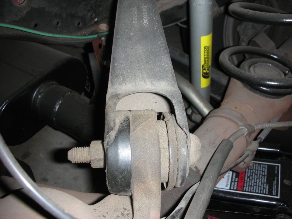 Suspension control arm with bushing, nut, and coil spring underneath vehicle