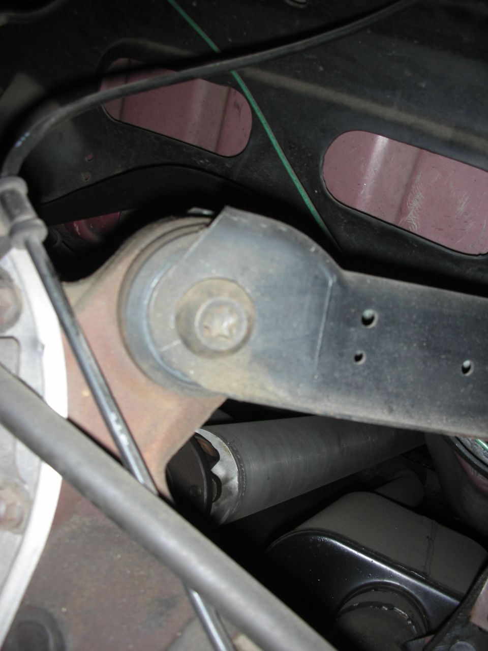 Suspension link arm bolted to bushing mount on dark vehicle underbody