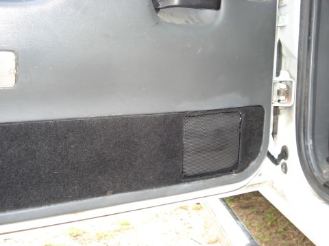 1992 Ford C-350 (Centurion Conversions) - Close-up of the lower half of a gray truck door panel with dark carpet trim and a black mesh speaker grille installed in a rectangular cuto…