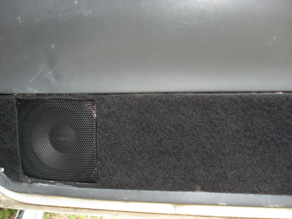 Close-up of a car door panel with a black speaker grille and dark carpet covering