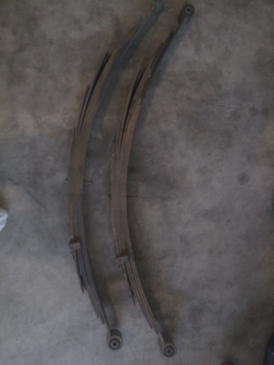 Pair of arched multi-leaf steel leaf springs with bushed eyes on a concrete floor