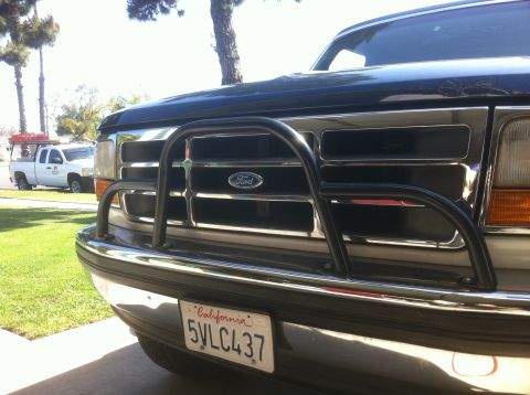 1995 Ford Bronco - Front view of a 1995 Ford Bronco a chrome grille and a black bull bar, with a white pickup truck in the background.