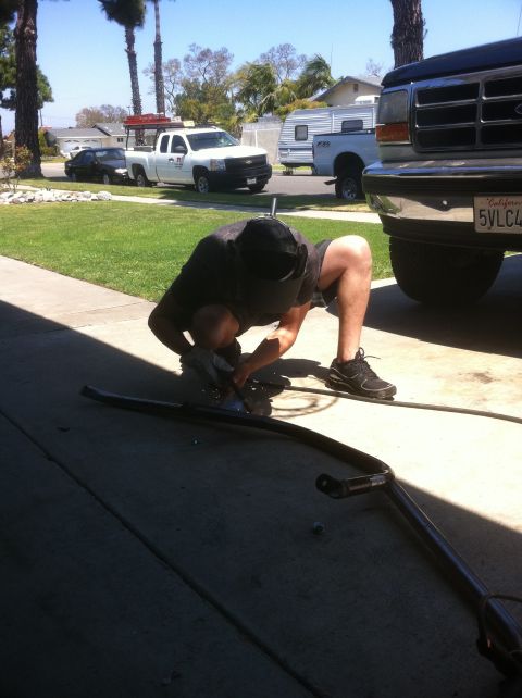 1995 Ford Bronco - A person is using a grinder on a metal bar in a driveway, with a truck and trailer visible.