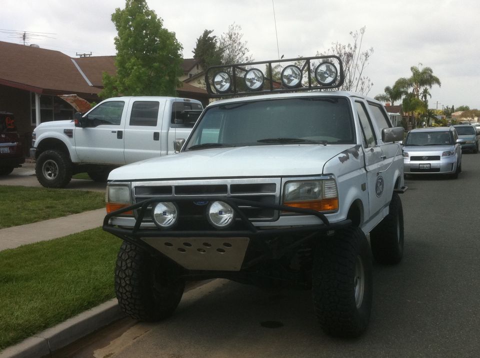 White Ford Bronco with a custom bumper, light bar, and lifted suspension parked on a street