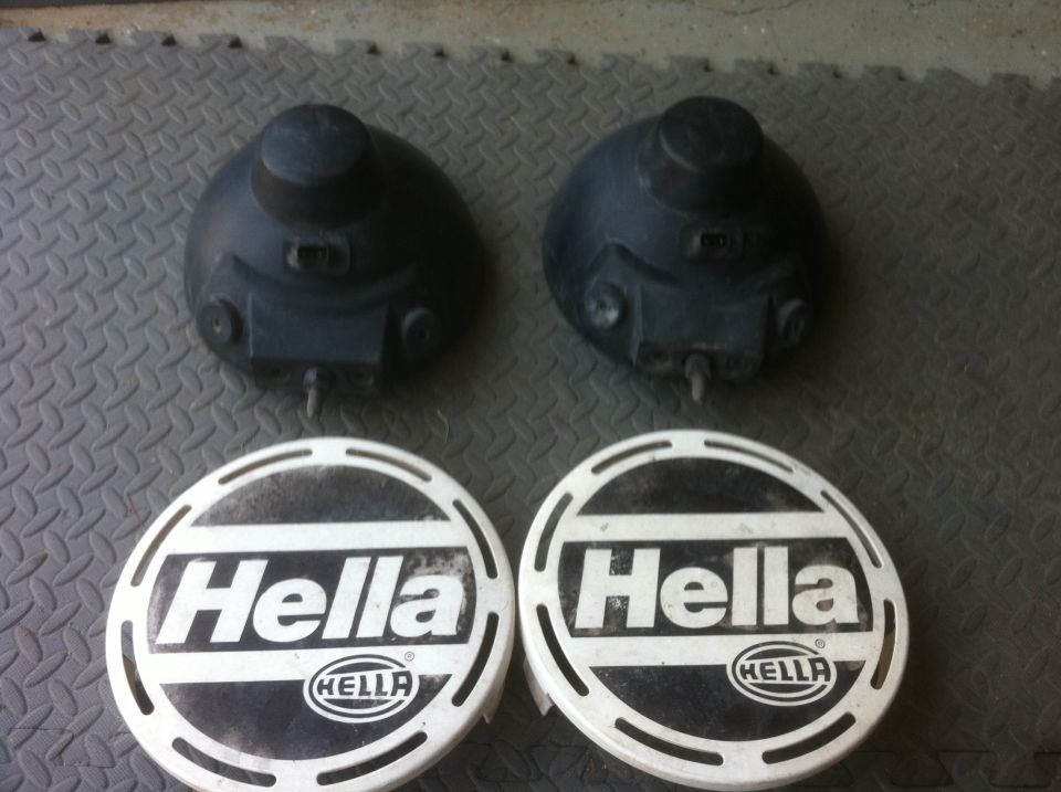 Two black Hella fog light housings and two white Hella fog light covers with text