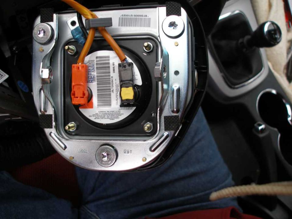 Steering wheel airbag module with orange and gray connectors, part of a car's interior
