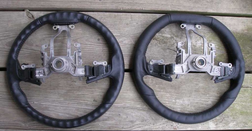 Two car steering wheels side-by-side on a wooden surface. One has smooth leather, the other perforated