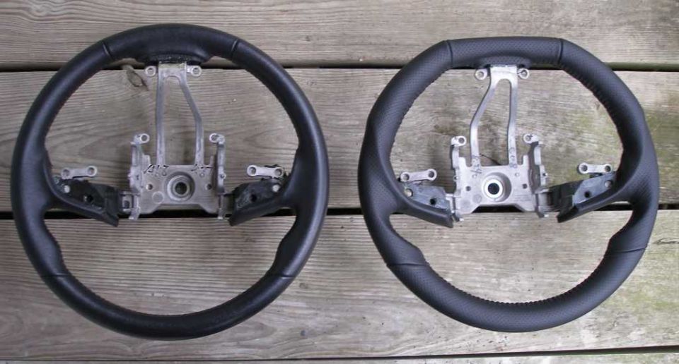 Two black steering wheels with metal mounting brackets against a wooden background