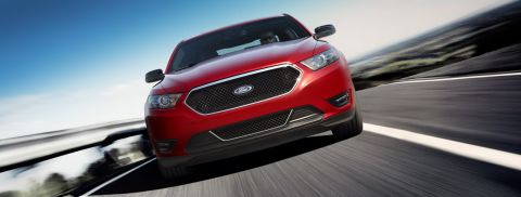 1993 Ford Taurus - A red Ford sedan is captured in motion on a highway under a bright blue sky.