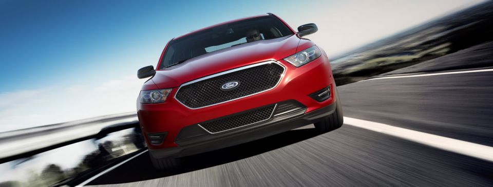 Red Ford sedan driving on a highway, front view