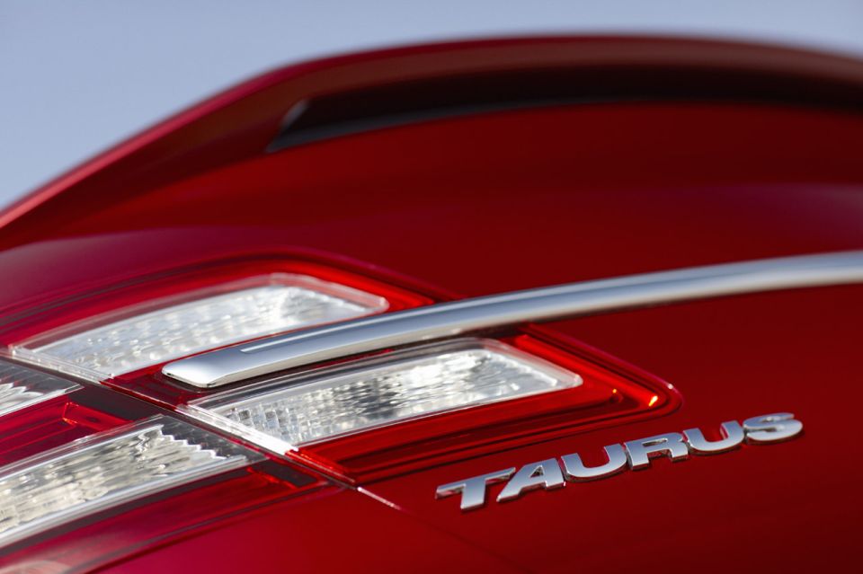Red car's rear with a chrome strip above the 'TAURUS' emblem and clear taillights
