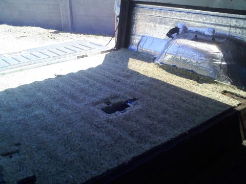 1994 Ford Bronco - The interior of a vehicle shows exposed insulation and a hole in the floor, with the tailgate open.
