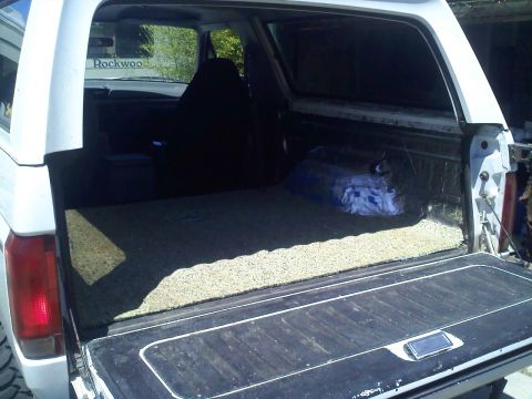 1994 Ford Bronco - Cargo bay of a white full-size SUV shot through the open tailgate, with the rear seat removed and fresh speckled sound-deadening or bedline…