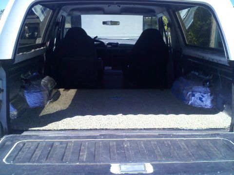 1994 Ford Bronco - Straight-on view through the open tailgate of a white full-size SUV with the rear seat removed, showing a speckled jute-and-foam sound insu…