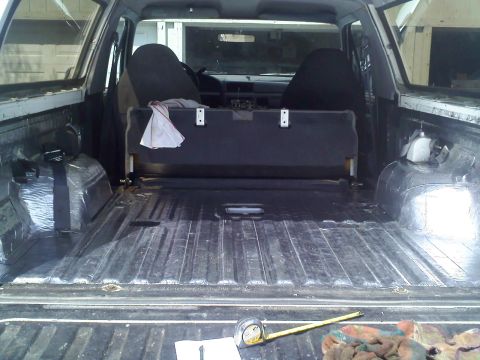 1994 Ford Bronco - Interior of a full-size SUV shot square through the open tailgate, with the carpet pulled and the ribbed cargo floor and wheel wells covere…